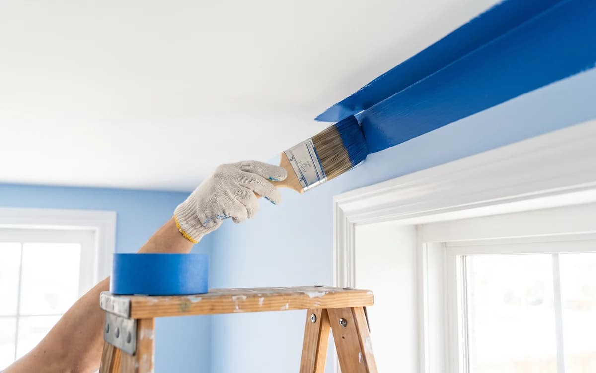 Handyman cutting in a blue accent ceiling line with a brush, interior painting
